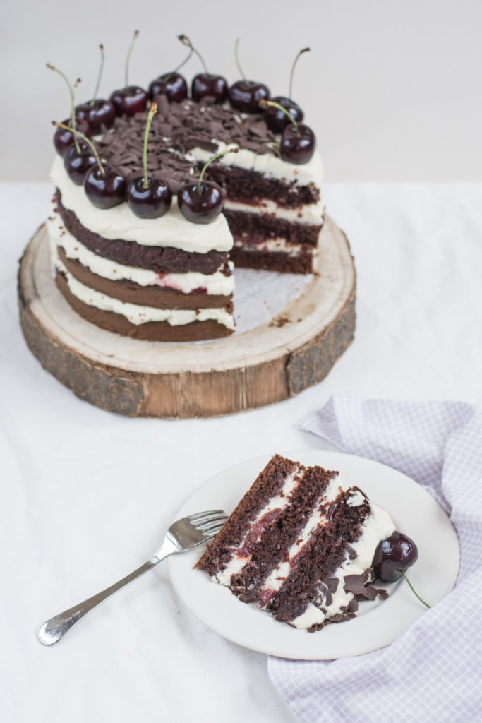 Dort Black Forest Cake ze tří čokoládových vrstev potřených třešňovým sirupem s griotkou, mascarpone krému a třešní, zdobený hoblinkami čokolády a třešněmi.